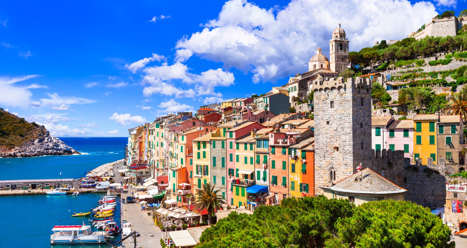 pogled na vas Vernazza, s pisanimi pročelji hiš, čolni na vodi in modrim morjem